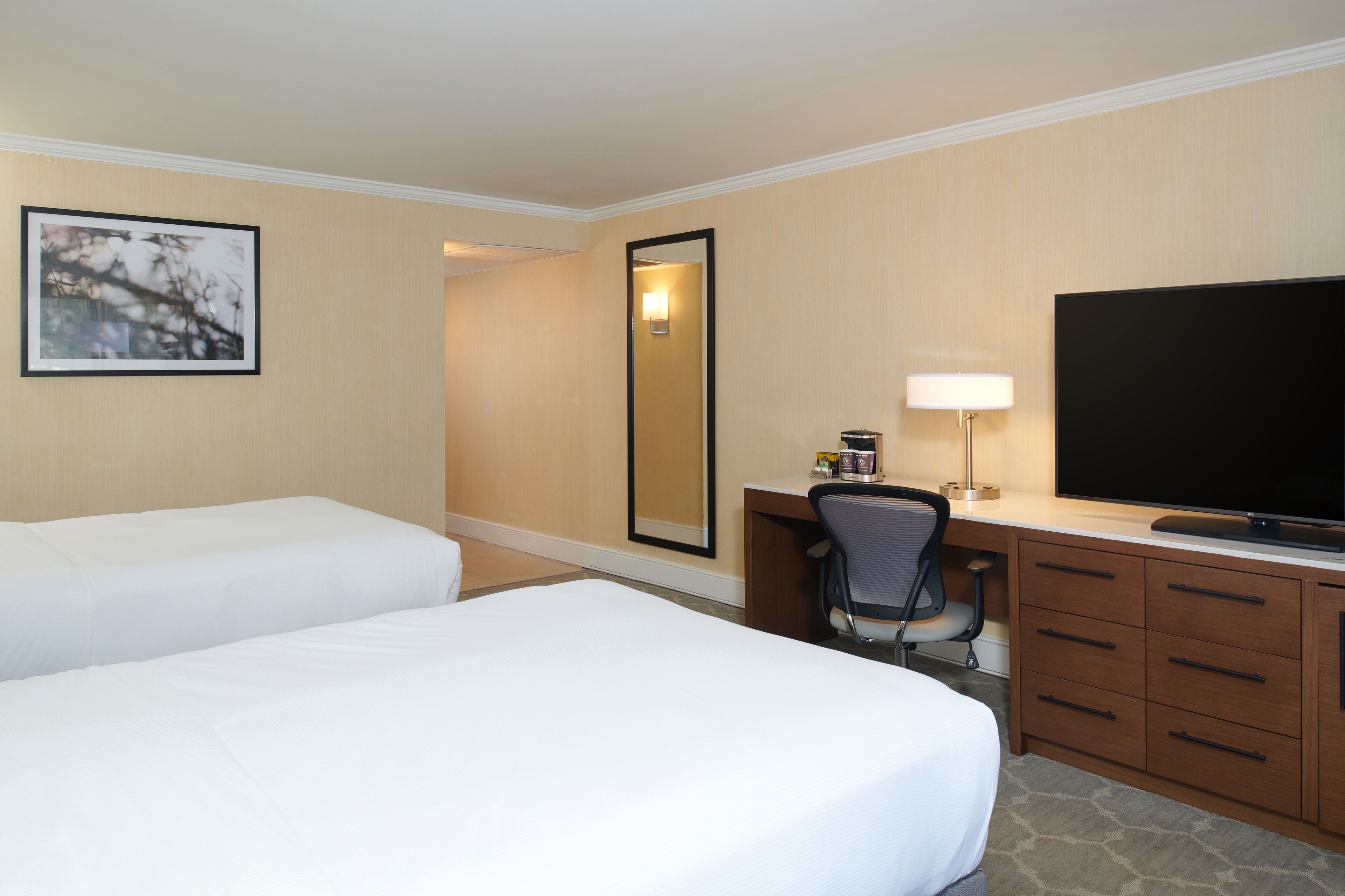 Une chambre d’hôtel avec deux lits, un bureau avec une chaise, une télévision et un miroir.