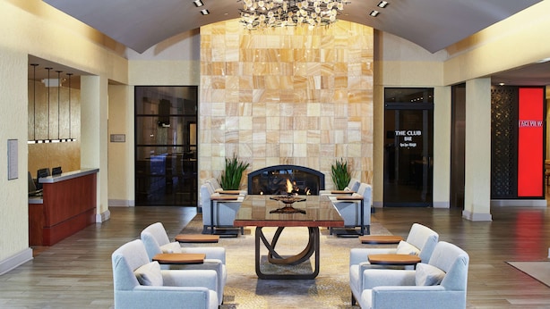A modern interior with a central dining table surrounded by six sofas, a fireplace, and a kitchen area visible through a glass partition. - DoubleTree by Hilton Hotel Salt Lake City Airport (Salt Lake City)