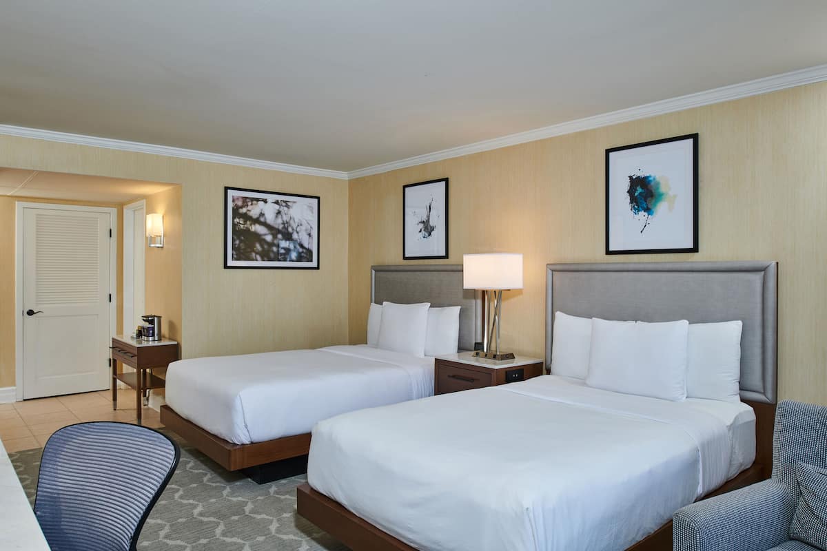 A hotel room with two beds, a desk, a chair, and artwork on the walls.