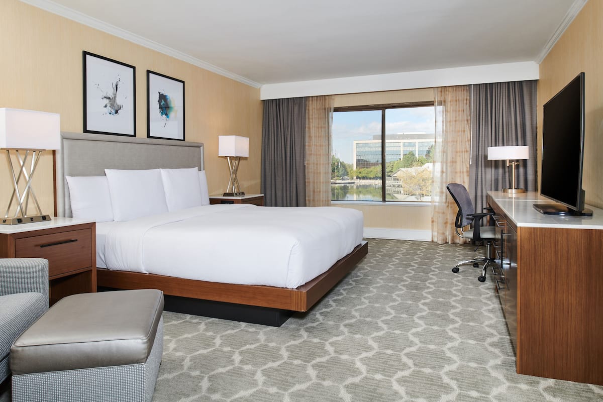 A hotel room with a large bed, a desk with a TV, a chair, and a view of a building through the window.
