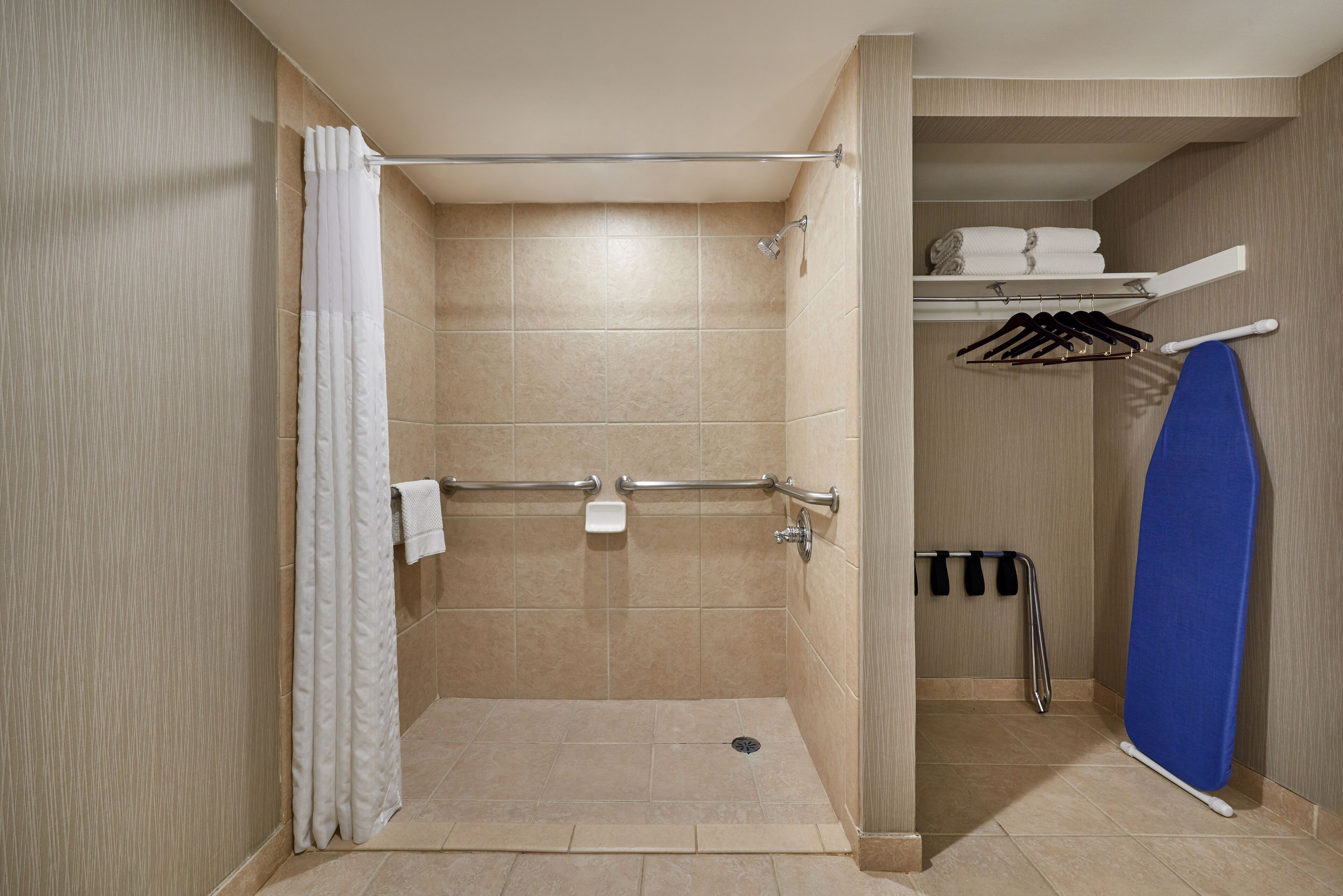A shower area with a grab bar, a towel rack, and a shelf with folded towels.
