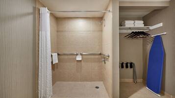 A shower area with a grab bar, a towel rack, and a shelf with folded towels.