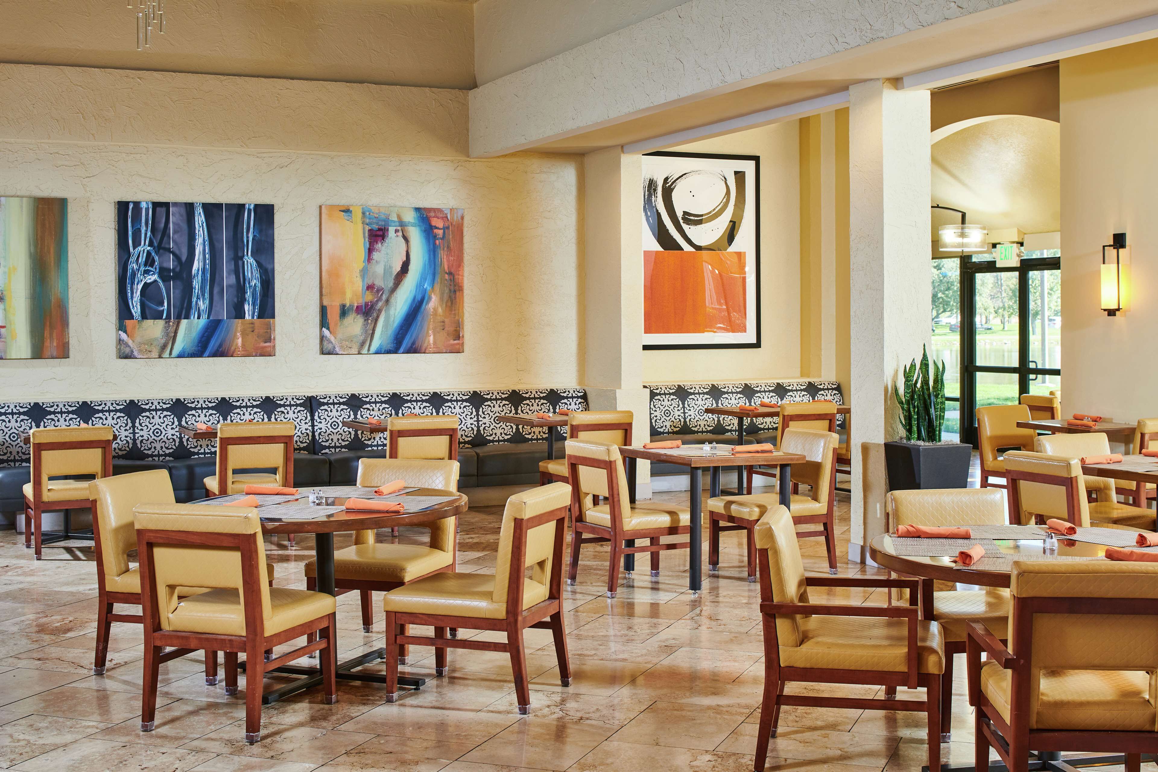Un restaurant avec des tables et des chaises en bois, des œuvres d’art abstrait accrochées aux murs et un motif décoratif sur les murs.
