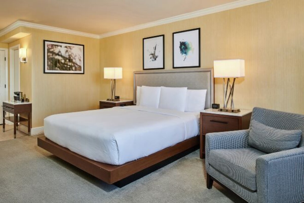 A hotel room with a large bed, two bedside tables, a chair, and framed artwork on the wall.