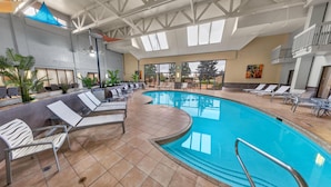 An indoor swimming pool with lounge chairs and a sunshade, surrounded by tiled flooring and large windows. - DoubleTree by Hilton Hotel Salt Lake City Airport (Salt Lake City)