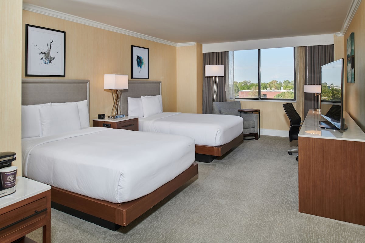 A hotel room with two beds, a desk, a chair, a TV, and a window with a view.