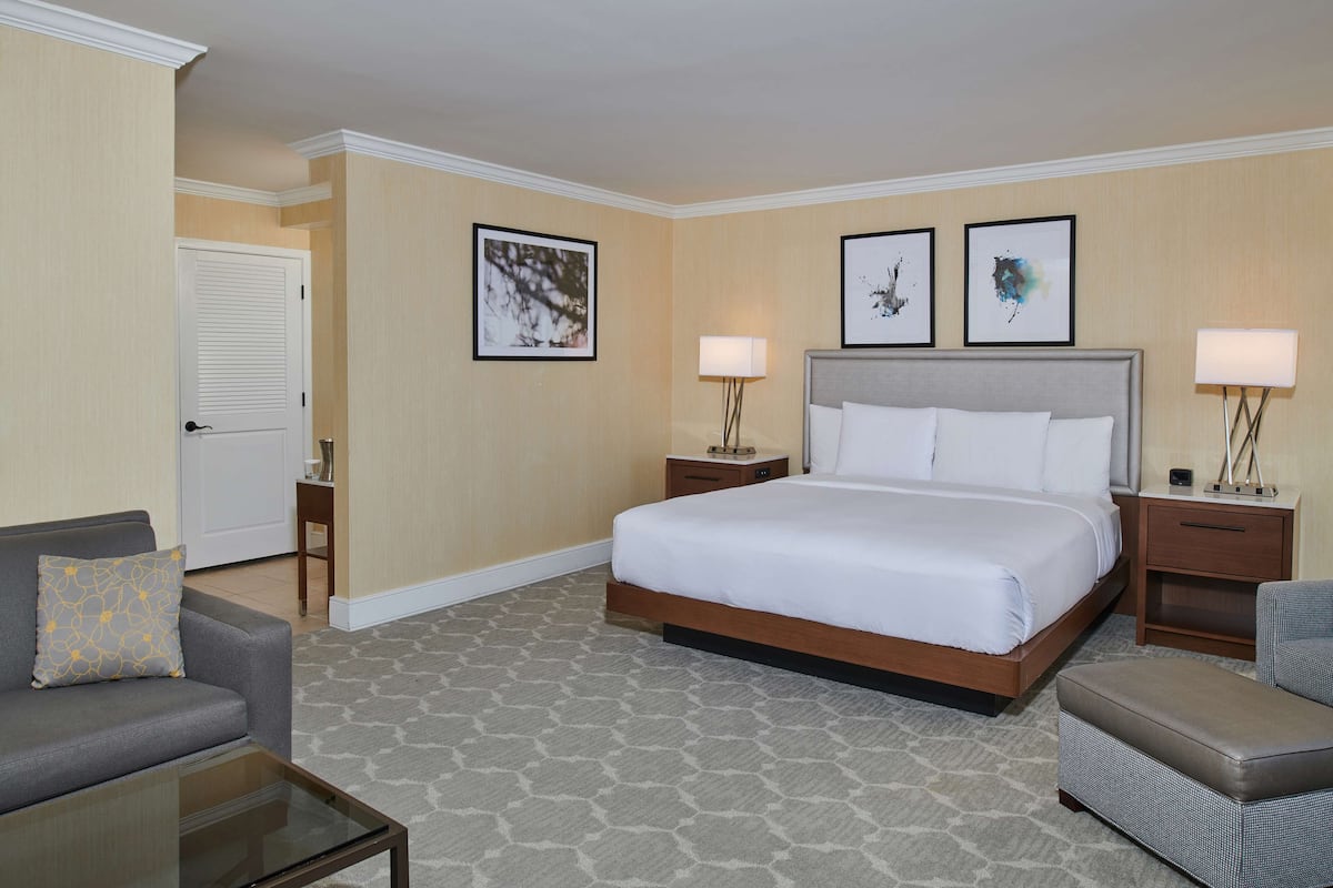 A hotel room with a large bed, two bedside tables with lamps, a sofa, a chair, and a small table.