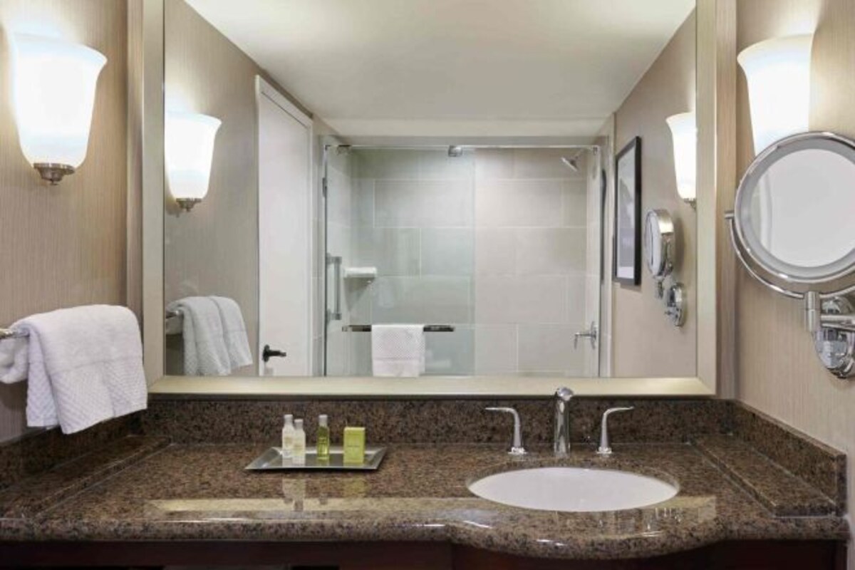 A hotel bathroom with a granite countertop, a sink, a mirror, and a glass shower enclosure.