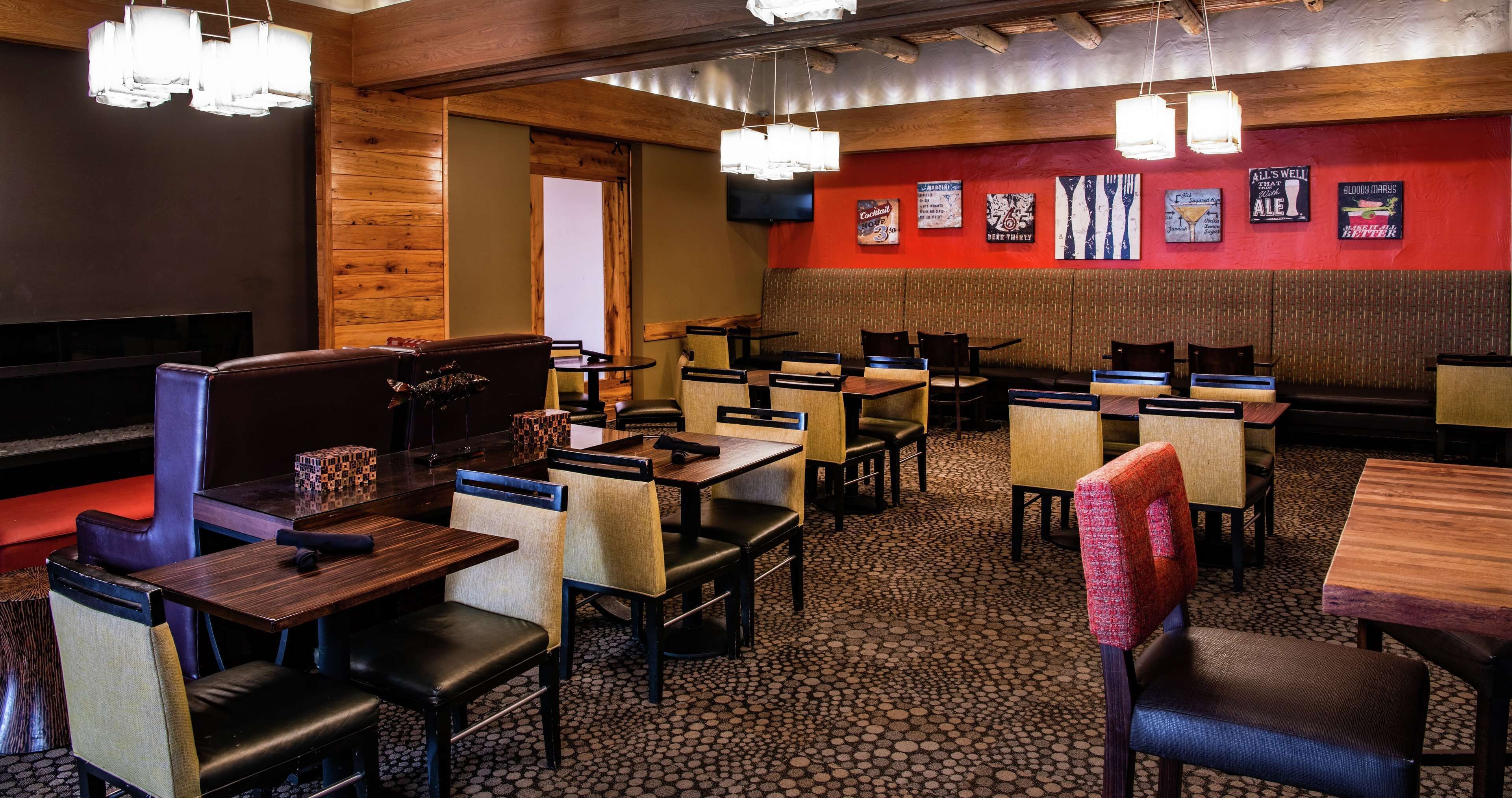 A restaurant interior with booths and tables, wooden walls, and a red accent wall with menu posters.