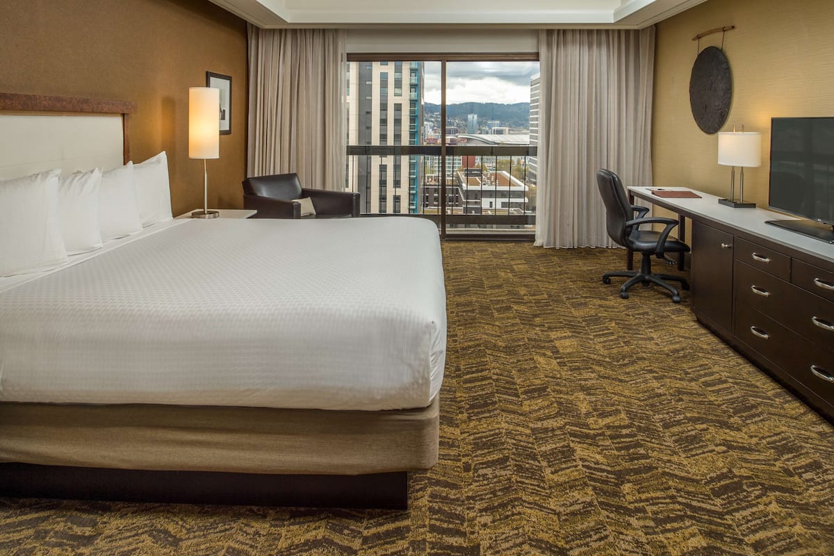 A hotel room with a large bed, a desk, a chair, and a TV.