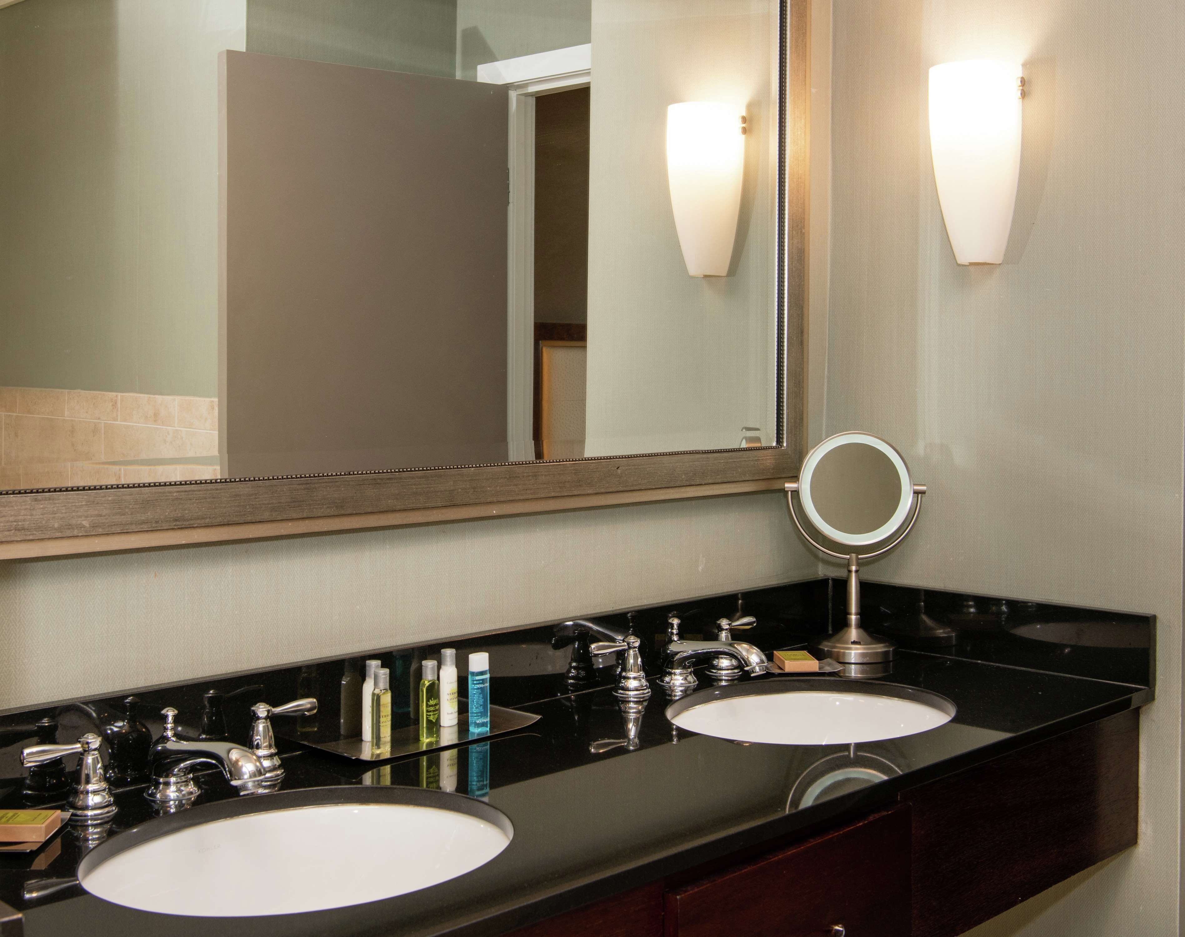 A bathroom with two sinks, a large mirror, and wall-mounted lights.