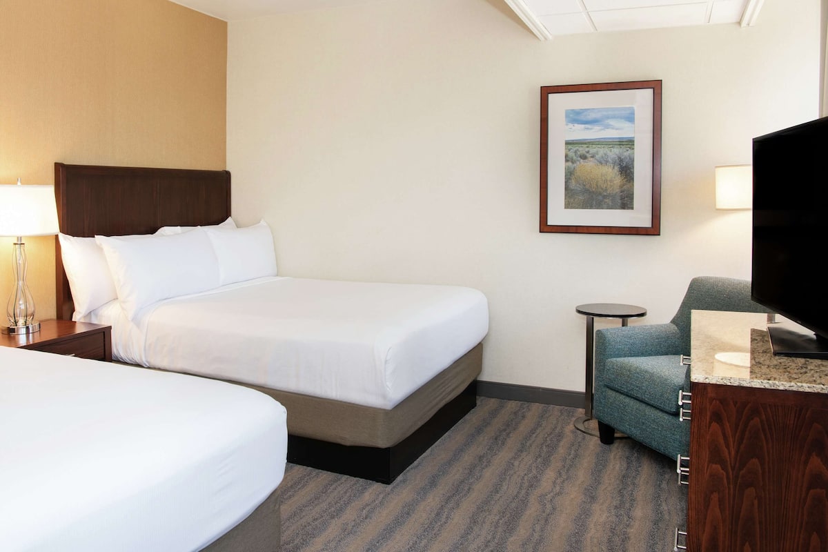 A hotel room with two beds, a television, a small table, and a framed picture on the wall.