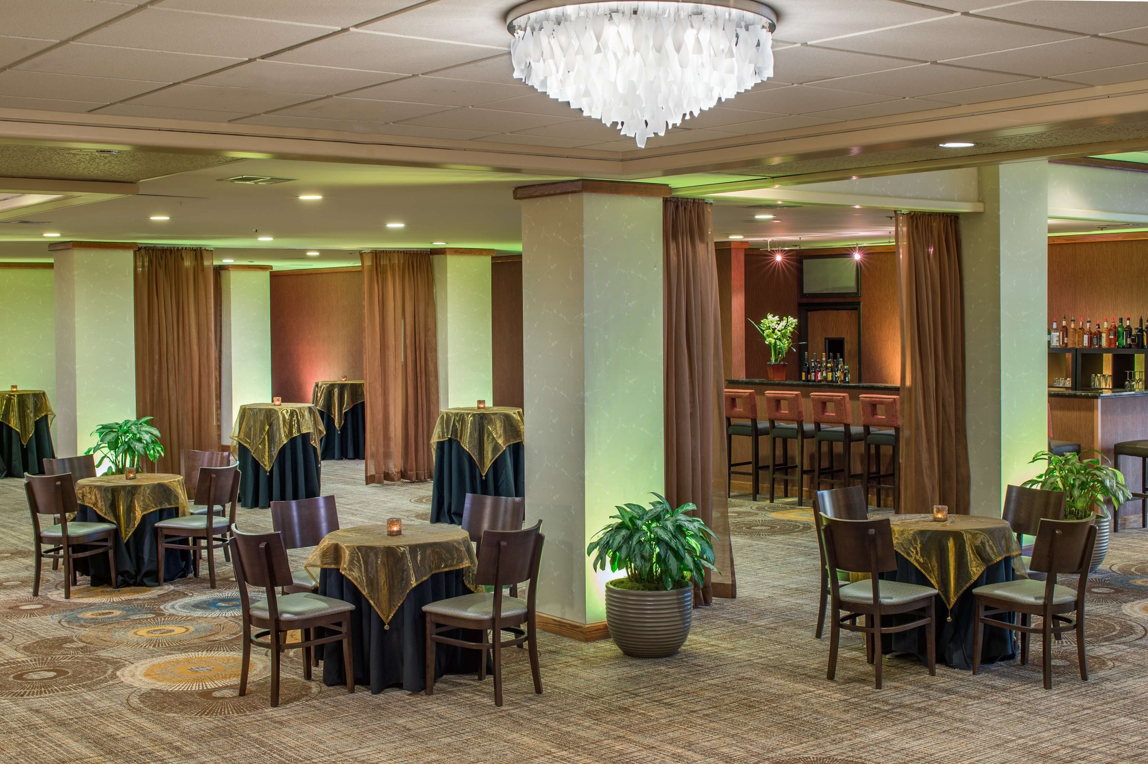 Una hall d'albergo con diversi tavoli e sedie, un'area bar e piante ornamentali.