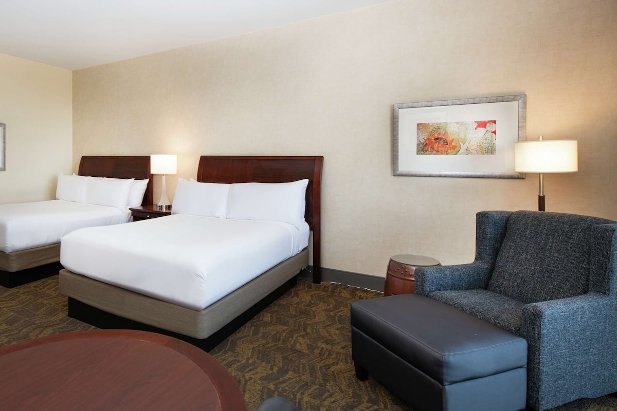 A hotel room with two single beds, a sofa, a small table, and a chair.