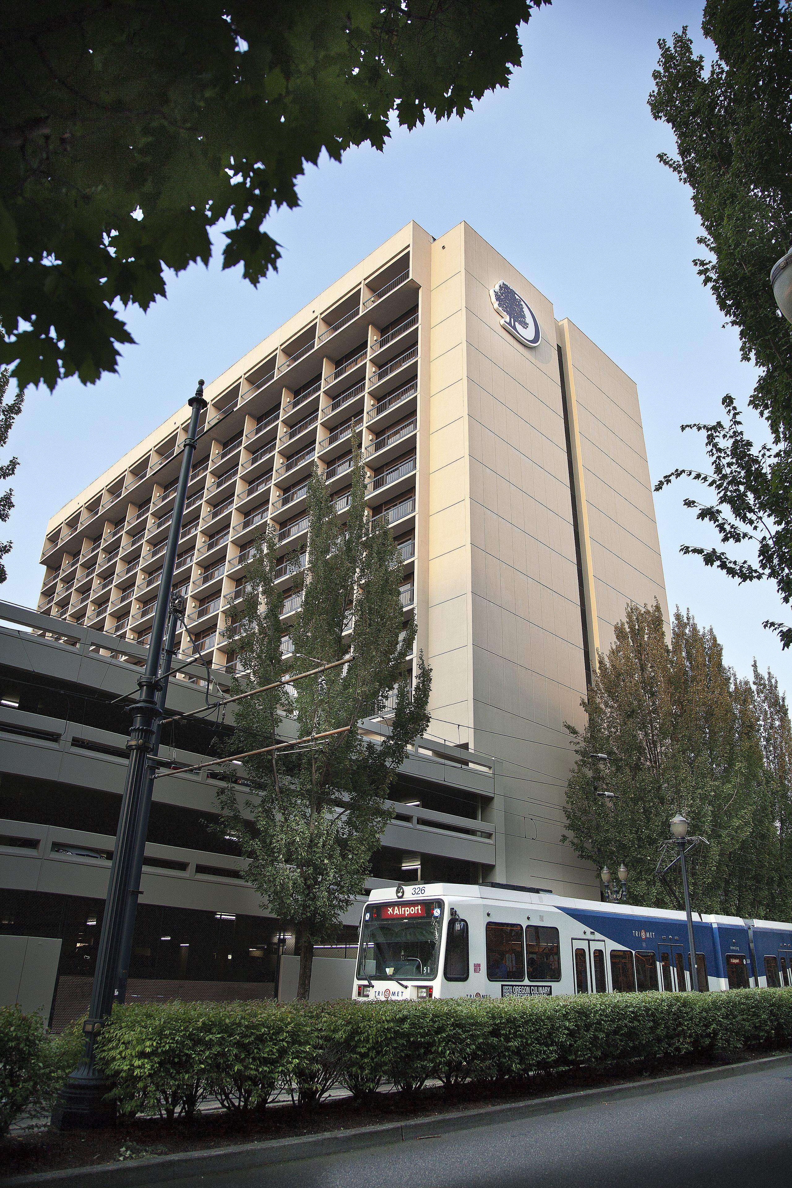 Un edificio moderno con un letrero grande, un estacionamiento y un tren que pasa.