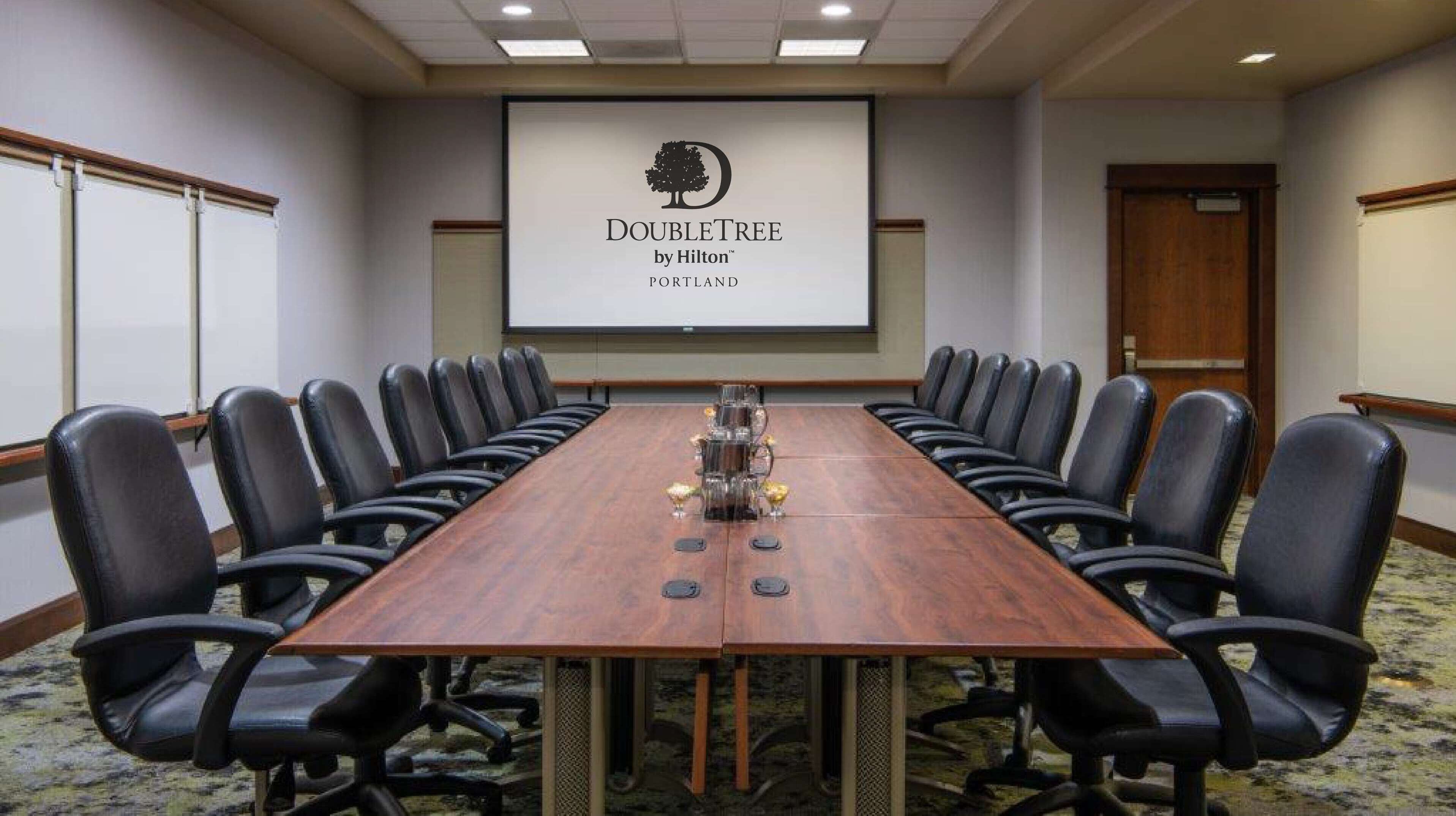 Una sala de conferencias con una larga mesa, sillas de cuero negro y una pantalla mostrando el logotipo de DoubleTree by Hilton.
