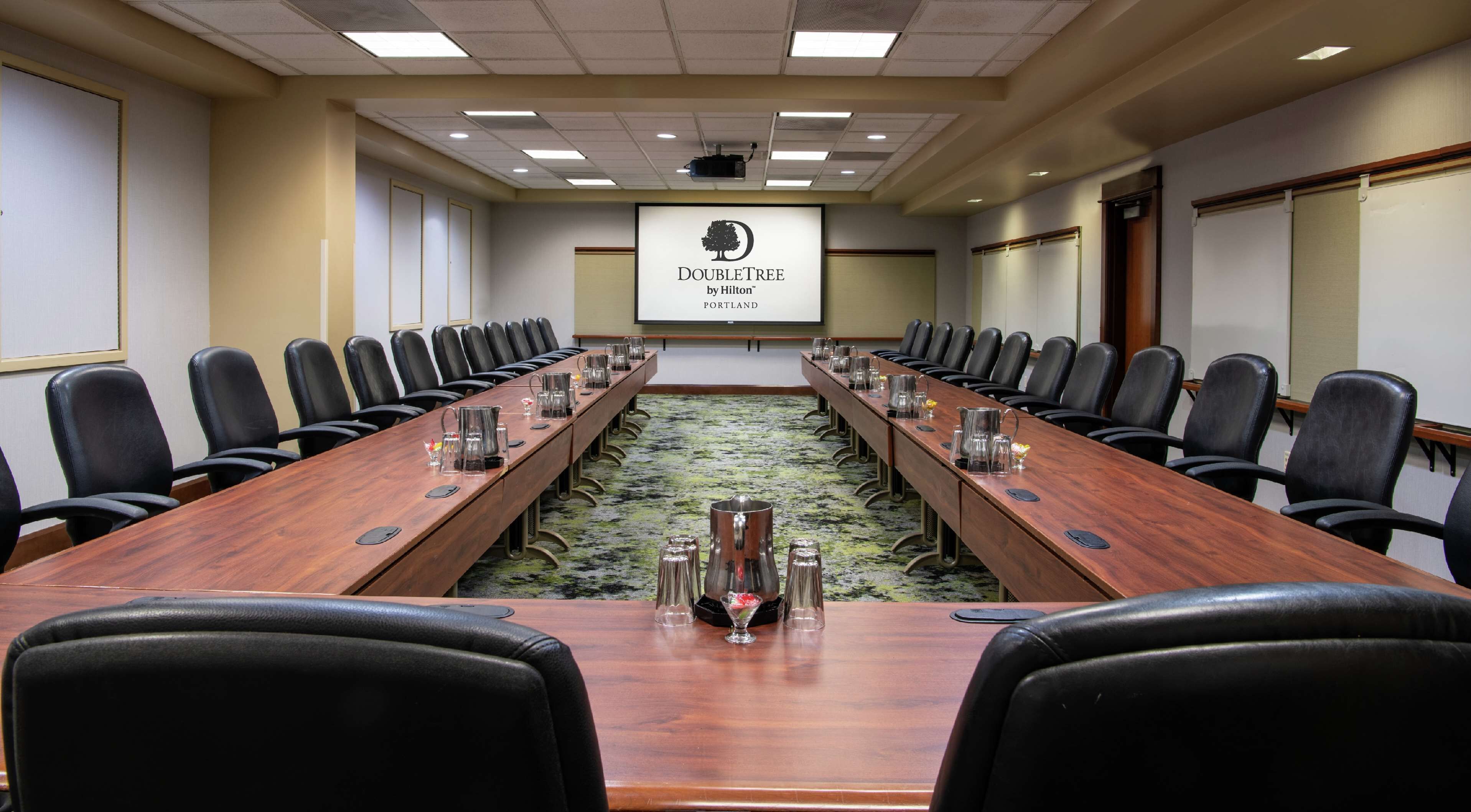 Une salle de conférence avec une longue table, des fauteuils en cuir noir et un écran de projection affichant le logo de la chaîne DoubleTree by Hilton.
