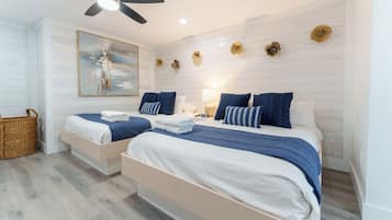 A hotel room with two beds, a ceiling fan, a painting, and decorative wall pieces.
