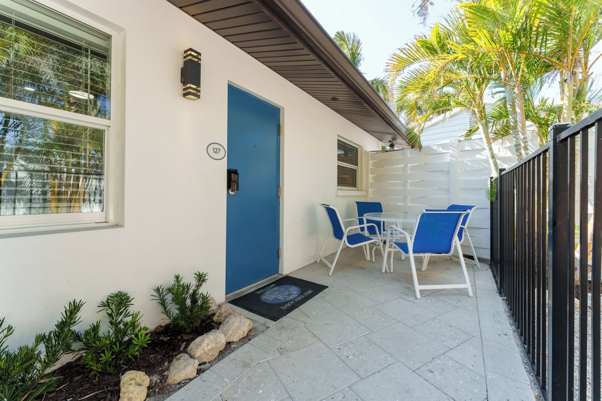A modern building with a blue door, a small patio with a table and chairs, and a black metal fence.