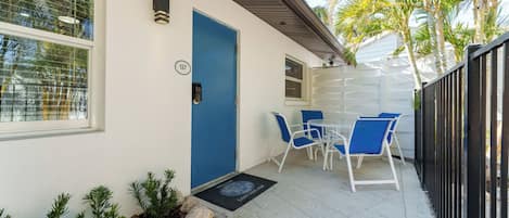 A modern building with a blue door, a small patio with a table and chairs, and a black metal fence.