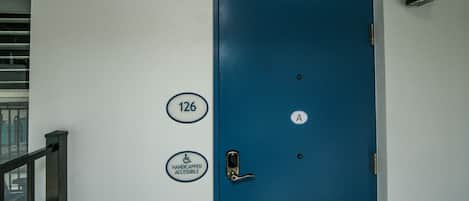Una puerta azul con señal de accesibilidad para personas con discapacidad, un letrero con el número de la habitación y un letrero con la letra 'A'.