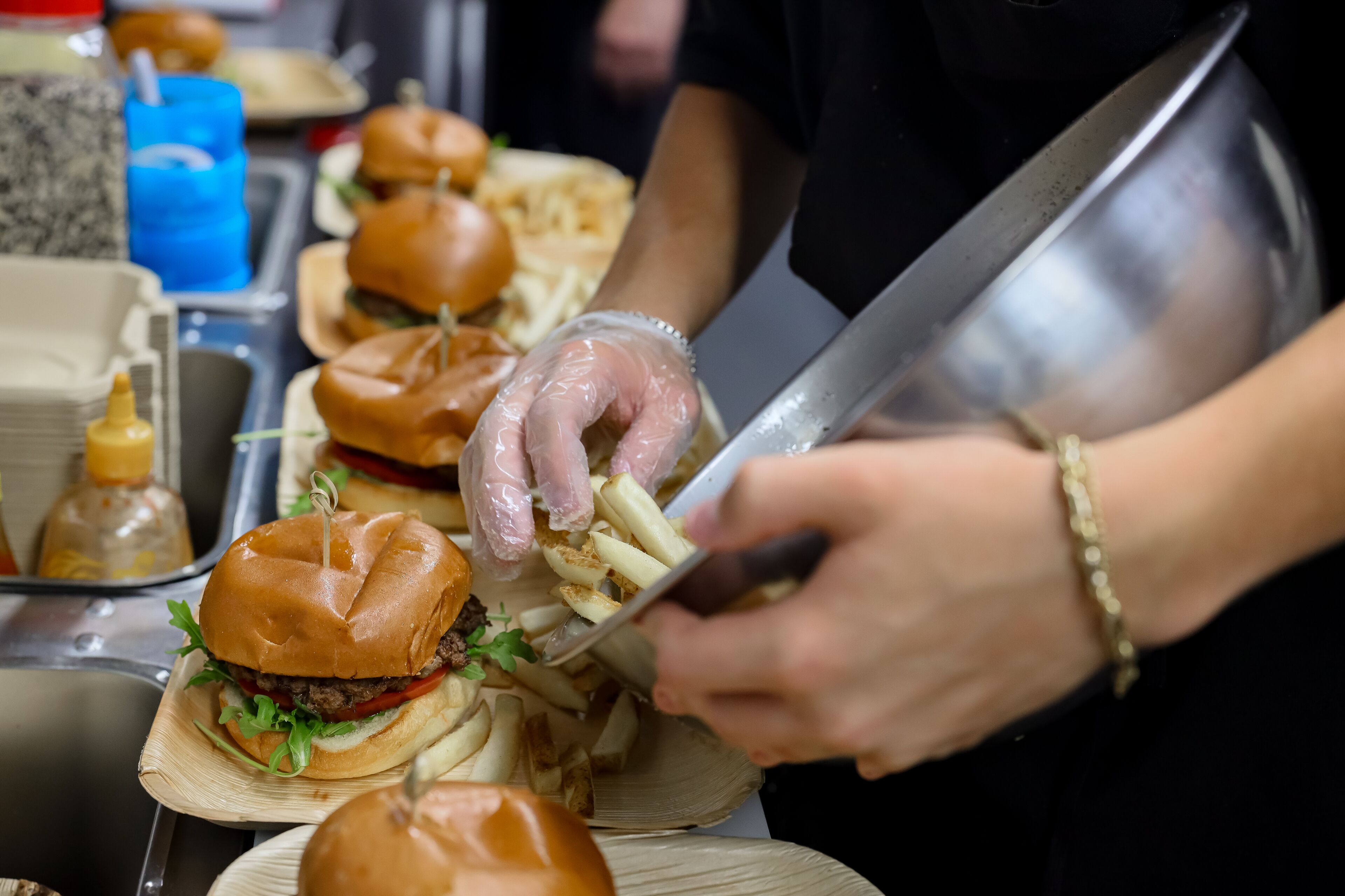 A person preparing food, specifically cutting fries, with a focus on the food preparation area.