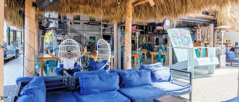 An outdoor seating area with blue cushioned sofas and tables, a thatched roof, and a sign for Big Tiko Lounge.