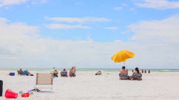 Une plage avec plusieurs chaises de plage et des parasols, une petite table et quelques personnes qui se détendent.