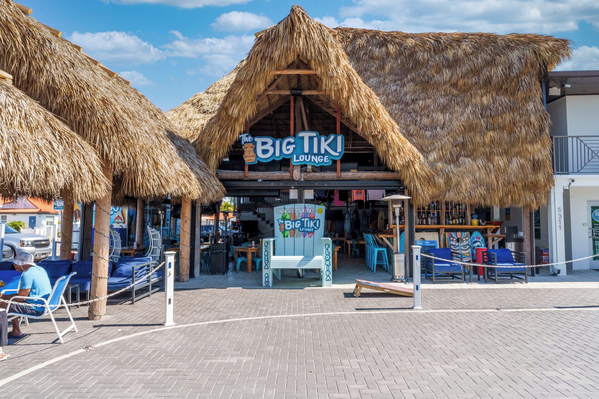 Rantakadun varrella sijaitseva oleskelutila, jossa on olkikatto ja kyltti, jossa lukee: ”The Big Tiki Lounge”.