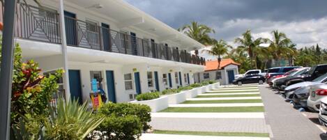 Un hotel con fachada blanca, varios balcones y un estacionamiento con coches.