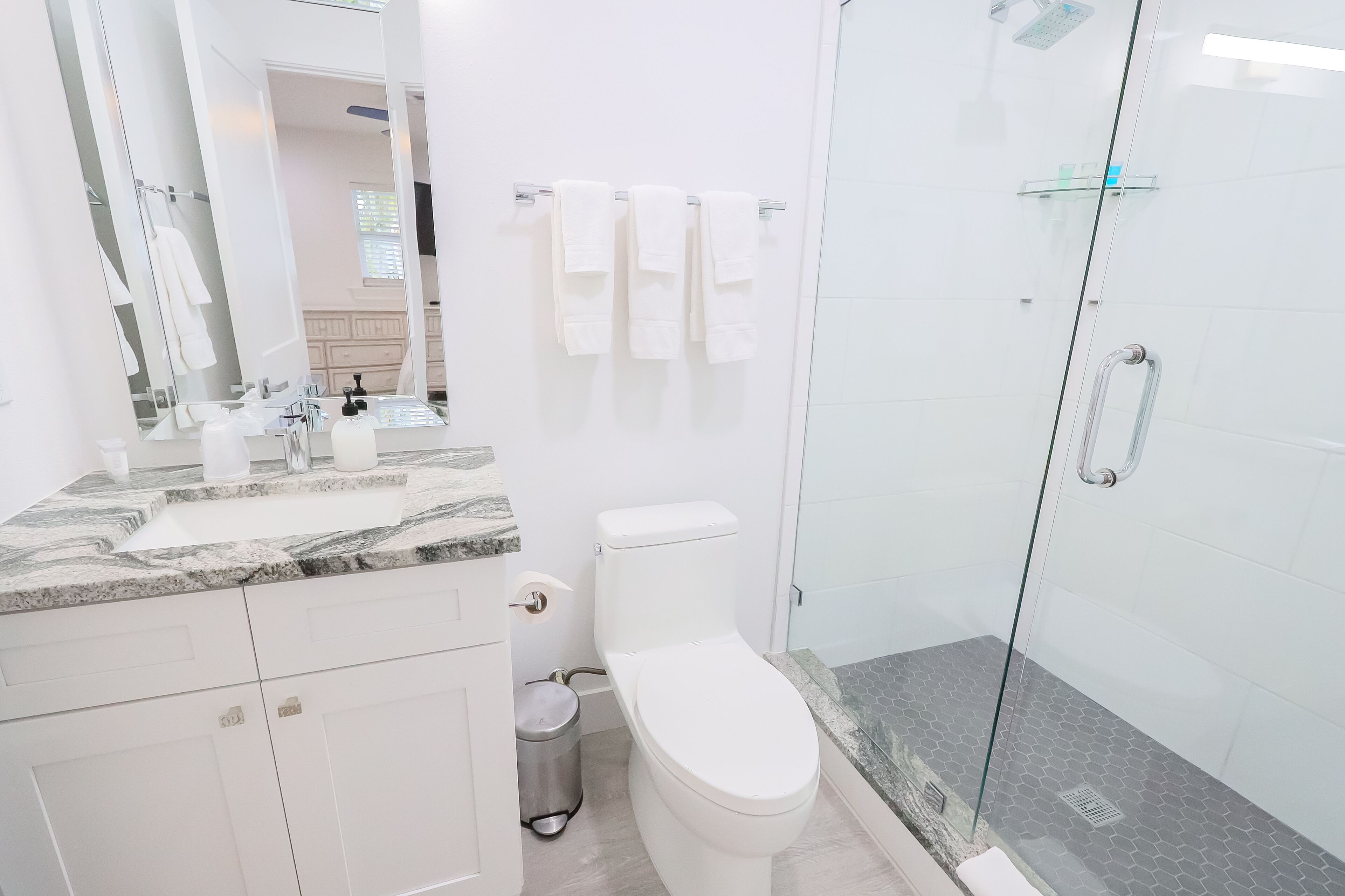 A modern bathroom with a glass-enclosed shower, a white toilet, and a marble countertop.