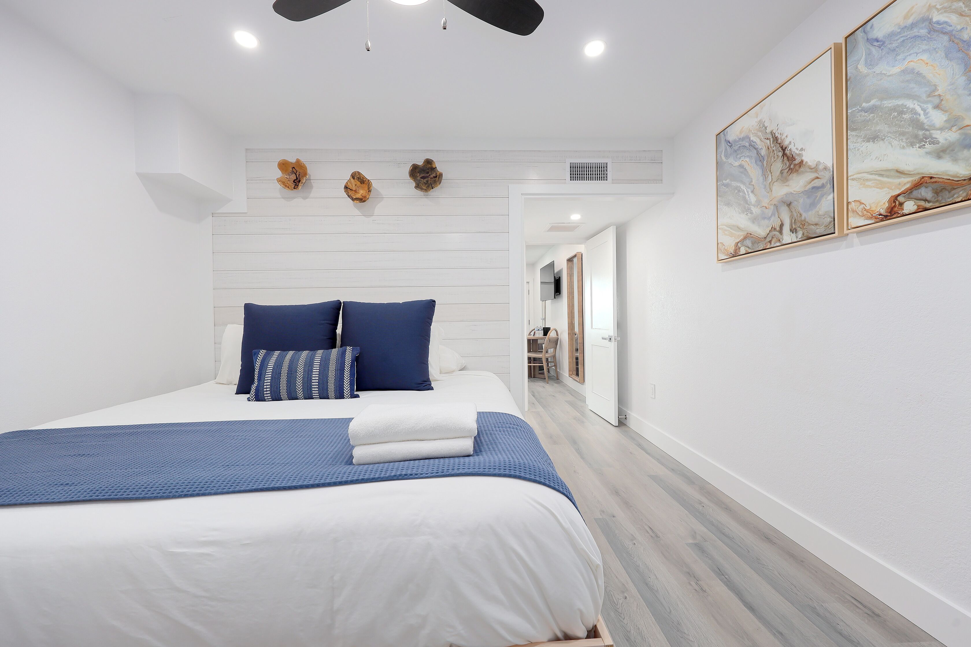 A modern bedroom with a bed, blue bedding, and a ceiling fan.