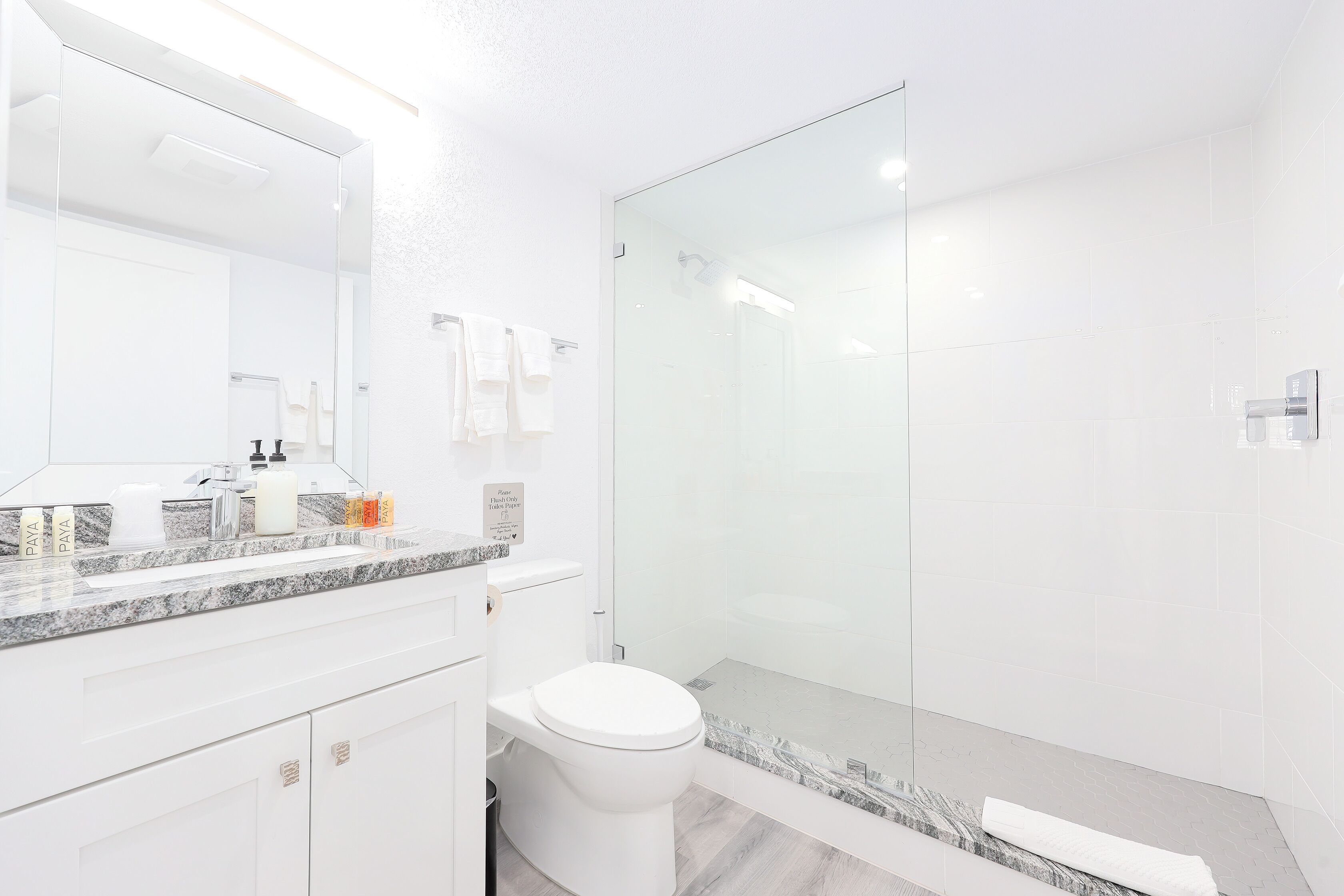 A modern bathroom with a white toilet, a glass shower enclosure, and a marble countertop.