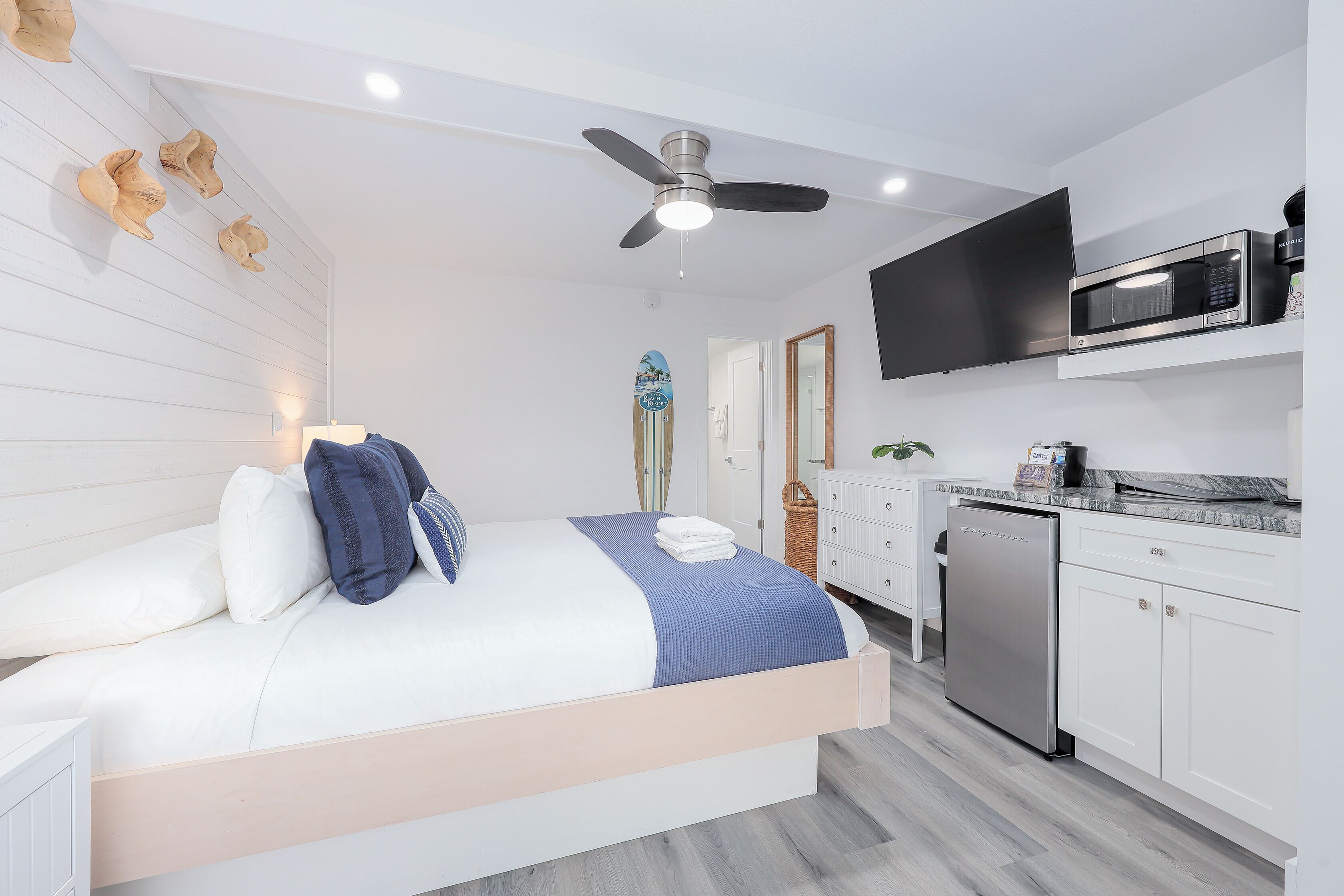 A modern bedroom with a bed, a ceiling fan, a microwave, and a dishwasher.