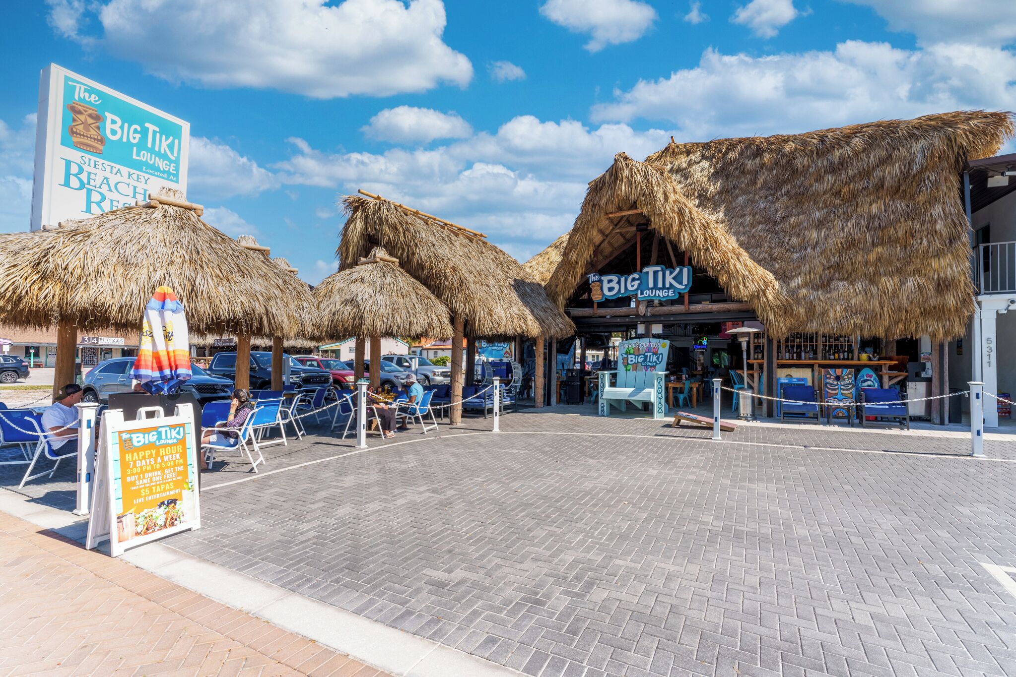Un salón junto a la playa con techos de paja y un cartel anunciando la hora feliz.