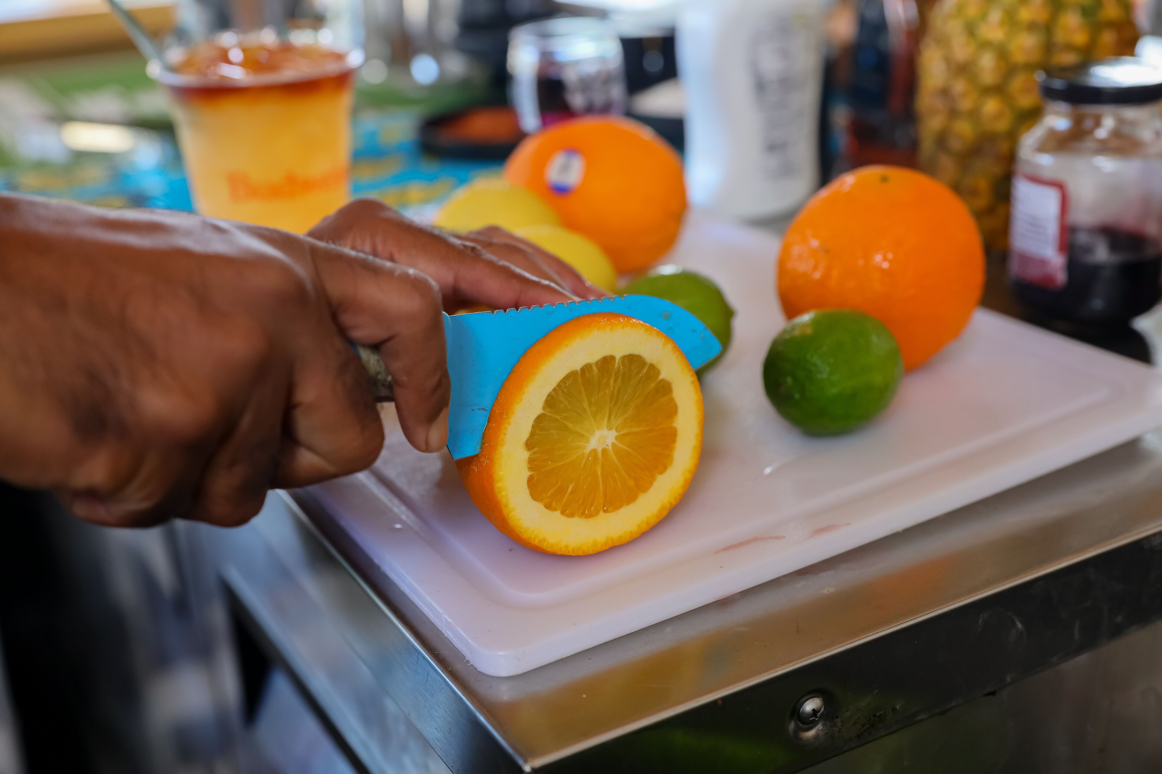 A hand using a blue cutter to slice an orange on a white cutting board.