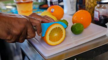 A hand using a blue cutter to slice an orange on a white cutting board.