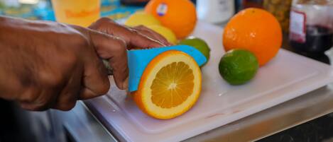 A hand using a blue cutter to slice an orange on a white cutting board.