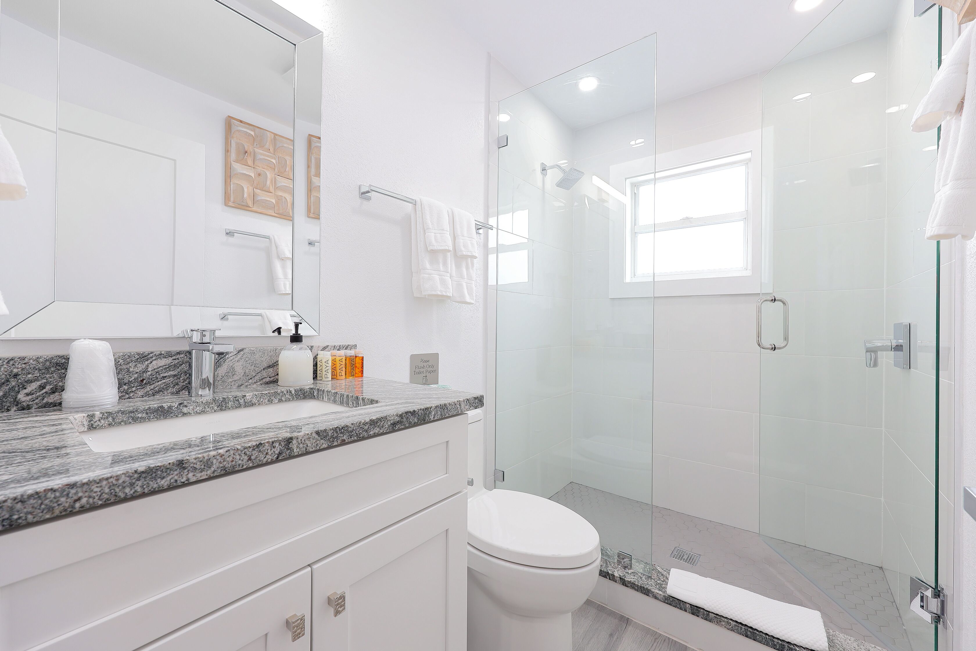 A modern bathroom with a glass-enclosed shower, a marble countertop, and a white toilet.