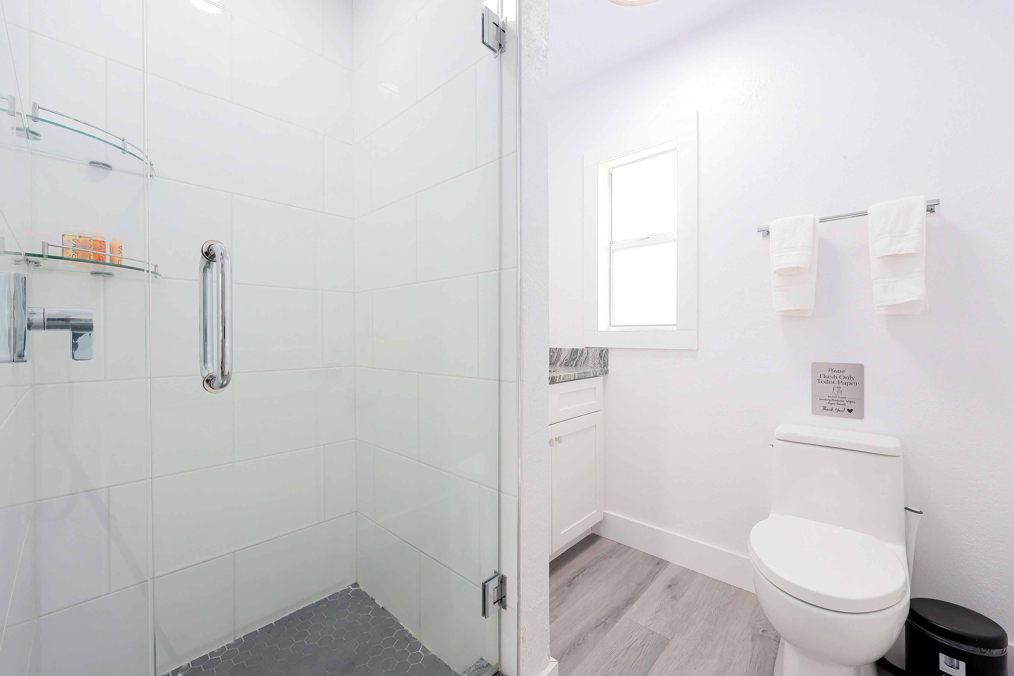 Ein modernes Badezimmer mit Duschabtrennung aus Glas, Toilette und kleinem Fenster.