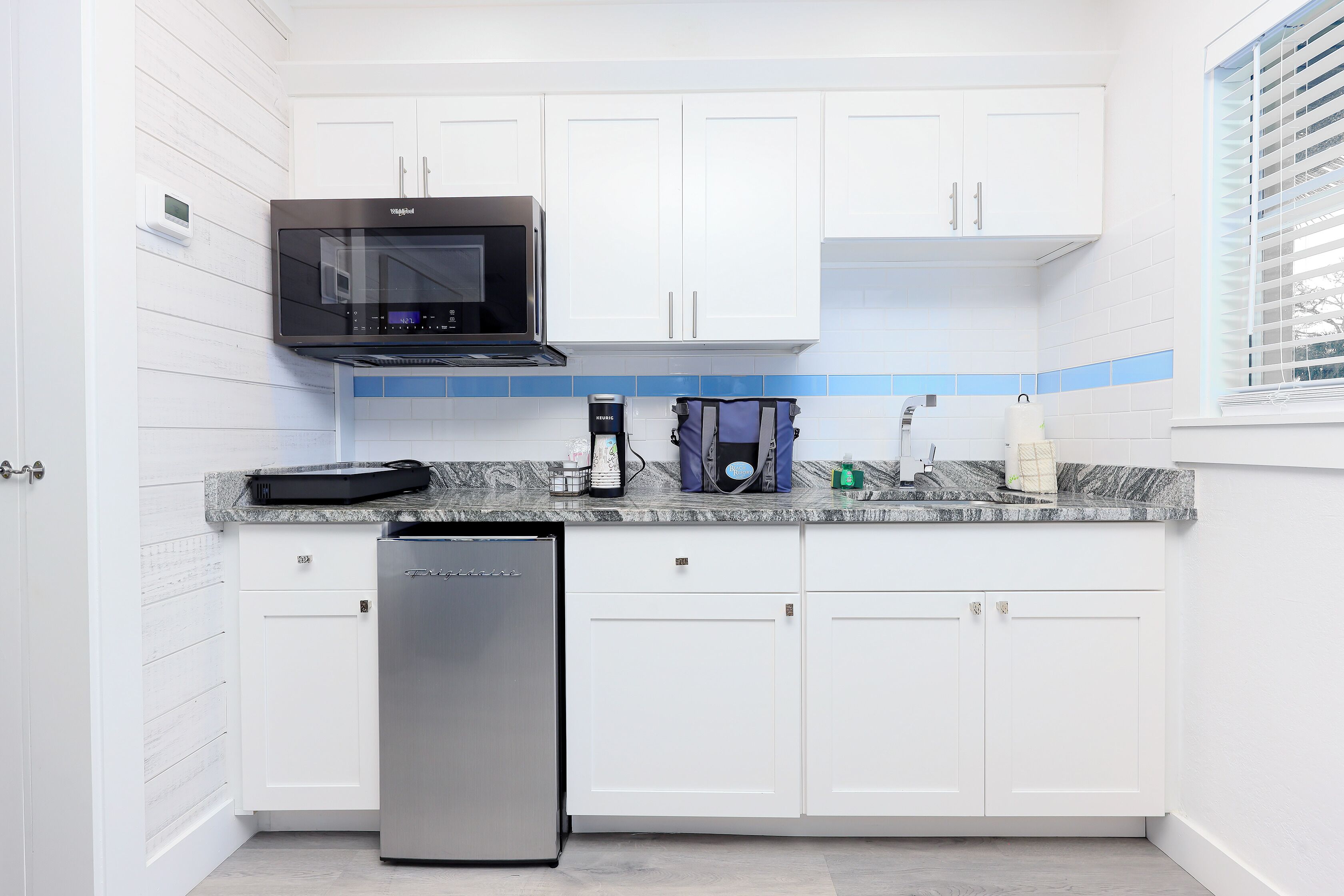 A modern kitchen with white cabinets, a stainless steel dishwasher, a black microwave, and a coffee maker on the countertop.