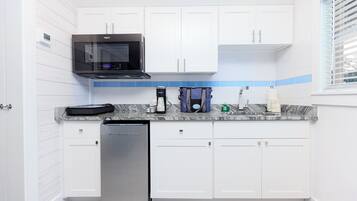 A modern kitchen with white cabinets, a stainless steel dishwasher, a black microwave, and a coffee maker on the countertop.