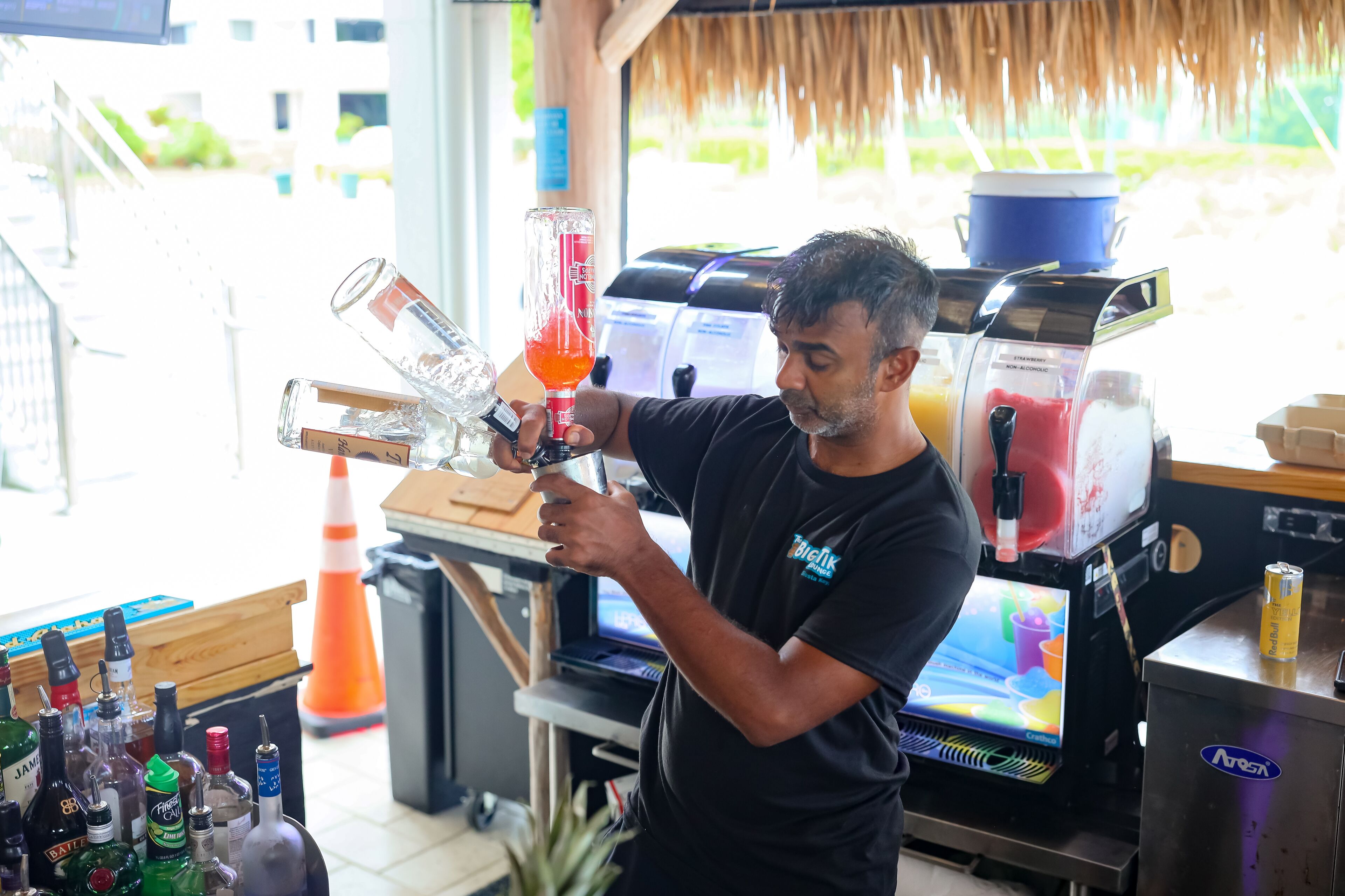 A barista preparing a drink with a coffee machine and various bottles in the background.