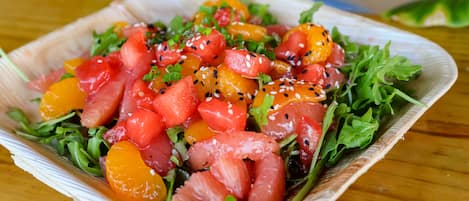 Ensalada con diversos vegetales y frutas sobre una mesa de madera.