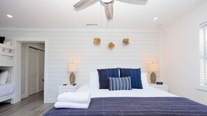 Une chambre à coucher comprenant un lit, deux tables de chevet, un ventilateur de plafond et une fenêtre avec des stores.