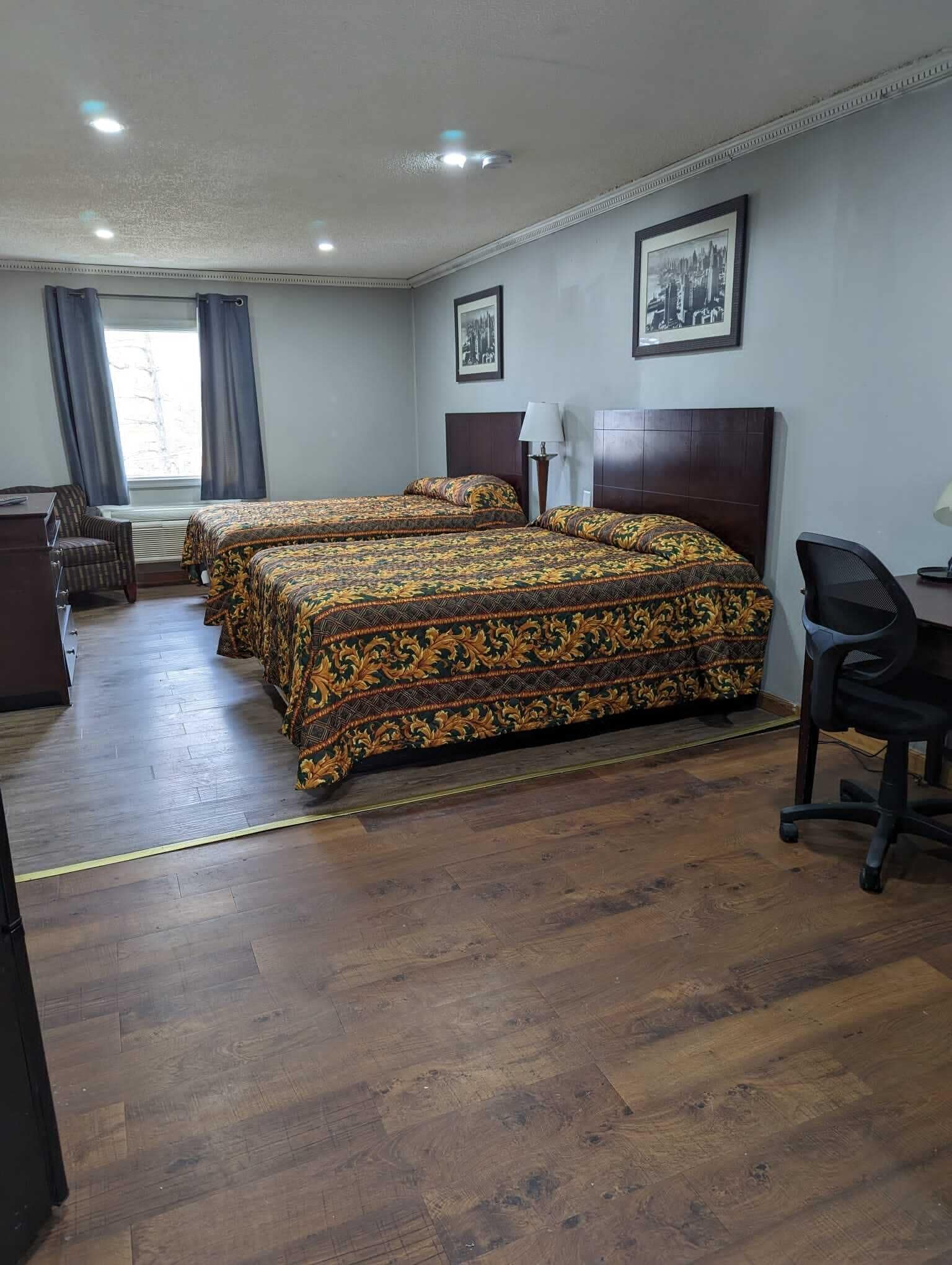 A hotel room with two beds, a desk, a chair, and a window with curtains.