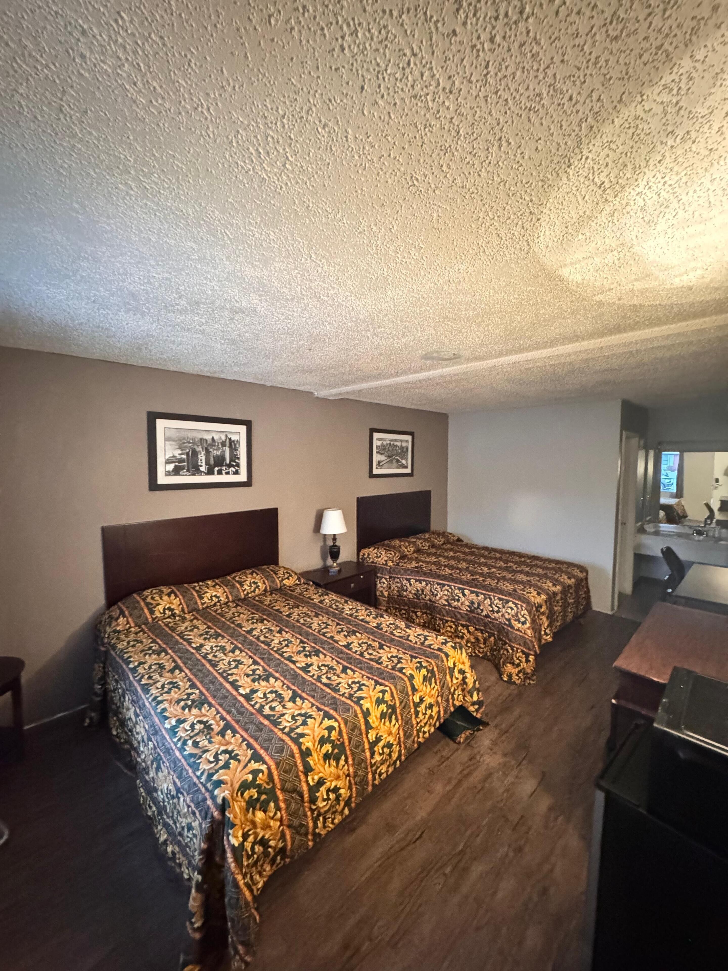 Habitación de hotel con dos camas, un escritorio y una silla. En la pared, hay fotografías enmarcadas.