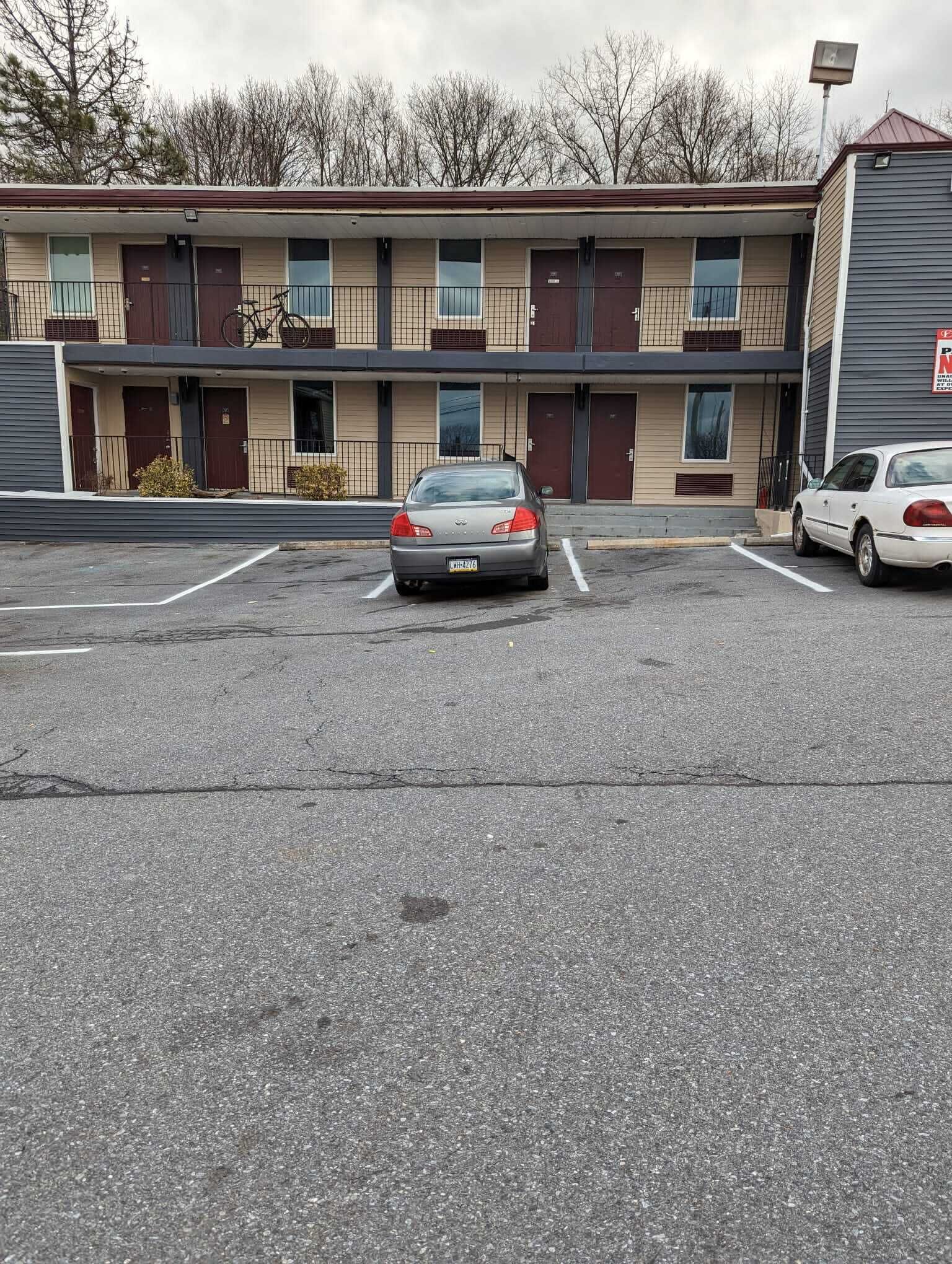 A parking lot with two cars, a building with multiple doors and windows, and a sign on the right.