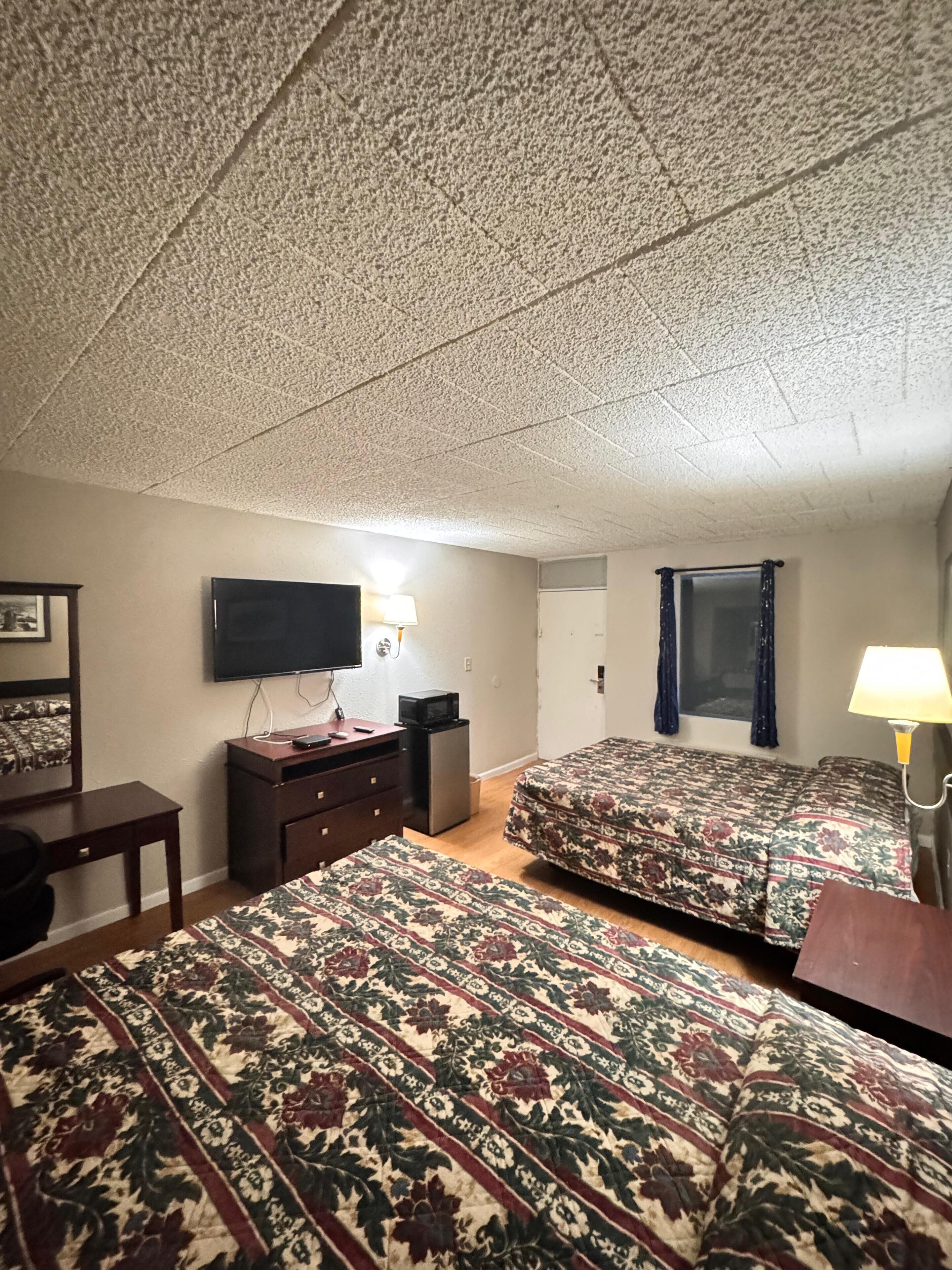 A hotel room with two beds, a TV, a desk, a lamp, and a mirror.