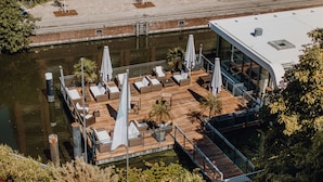 Un bar situé sur le toit d’un immeuble, avec des chaises longues et des parasols, offrant une vue sur une étendue d’eau.